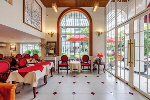 Un comedor de hotel con mesas dispuestas para los huéspedes, un amplio ventanal con vistas a la calle e iluminación empotrada en el techo.