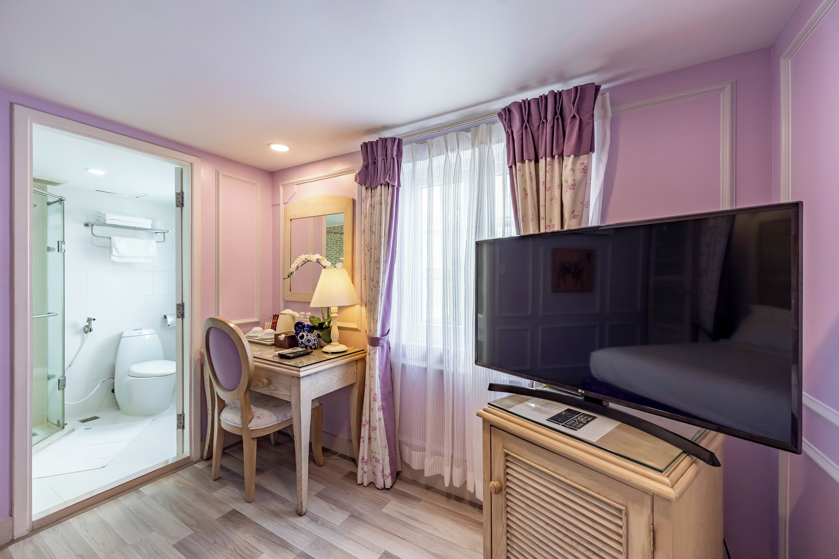 Habitación de hotel con ducha, inodoro, escritorio, silla, televisor y cortinas.