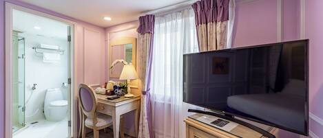 Habitación de hotel con ducha, inodoro, escritorio, silla, televisor y cortinas.
