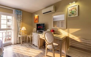 Habitación de hotel con escritorio, silla, televisor, aire acondicionado y ventana con cortinas.