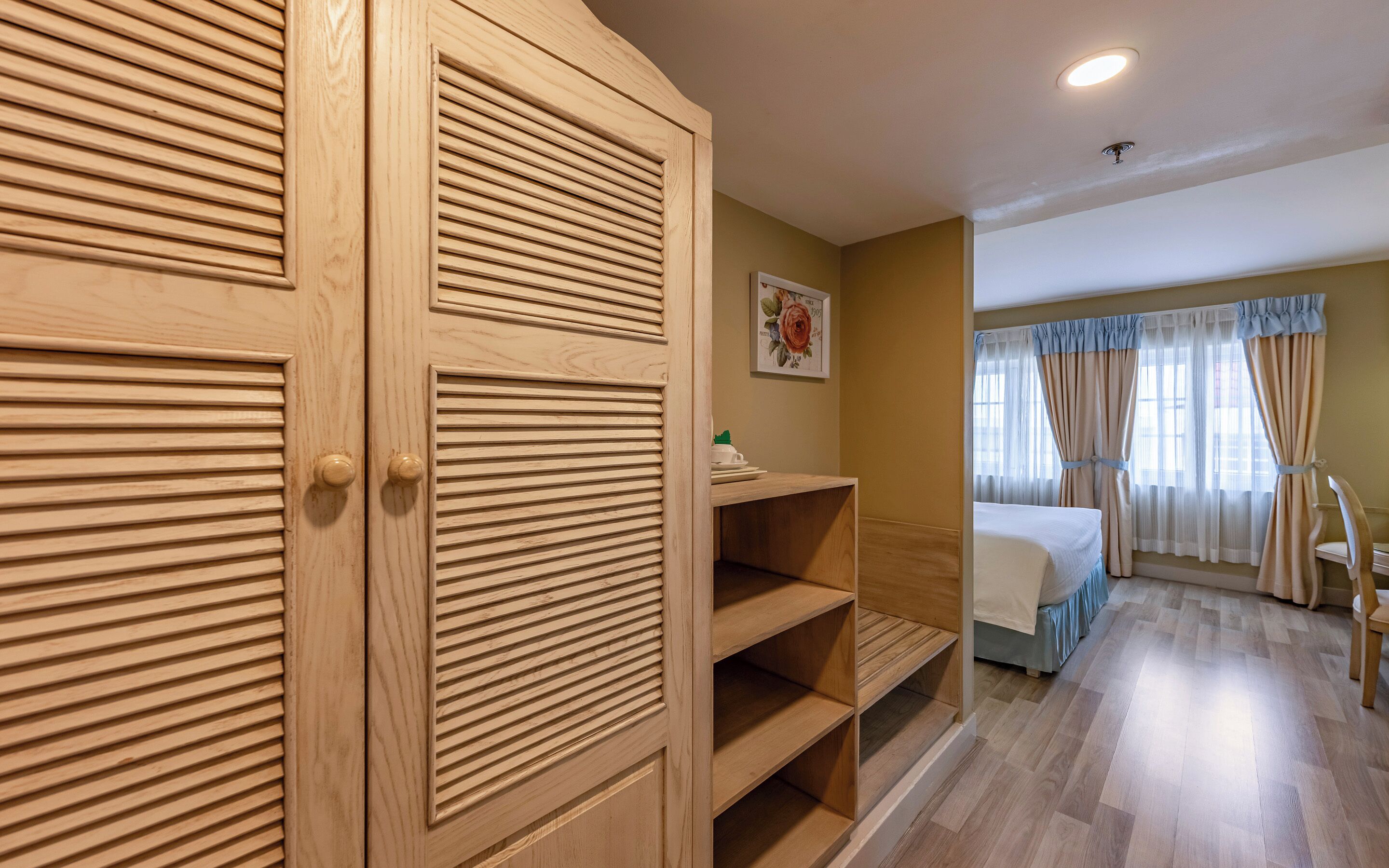 Habitación de hotel con armario de madera, cama con cubrecama azul y ventana con cortinas.