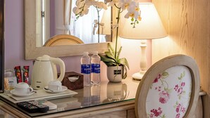 A hotel room with a wooden desk, a mirror, a floral chair, a lamp, and a vase with white orchids. - Hotel L Odeon Phu My Hung (Ho Chi Minh City)