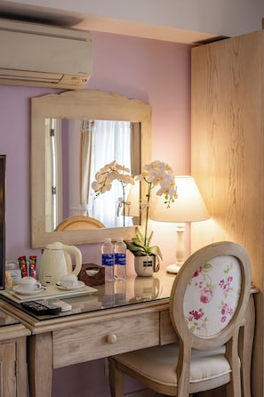 A hotel room with a wooden desk, a mirror, a floral chair, a lamp, and a vase with white orchids. - Hotel L Odeon Phu My Hung (Ho Chi Minh City)