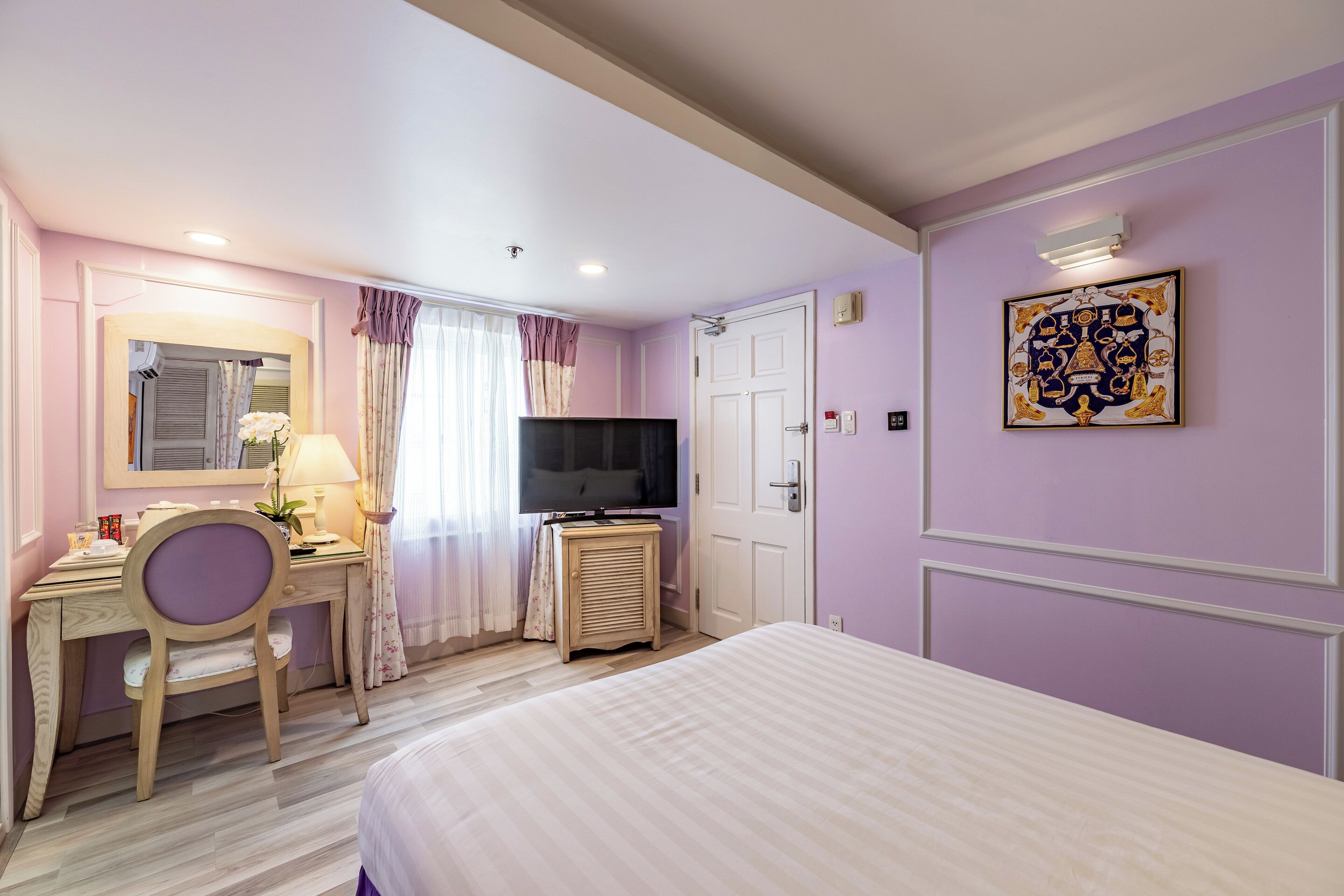 Een hotelkamer met een bed, bureau met stoel, televisie en een deur.