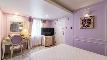 Een hotelkamer met een bed, bureau met stoel, televisie en een deur.