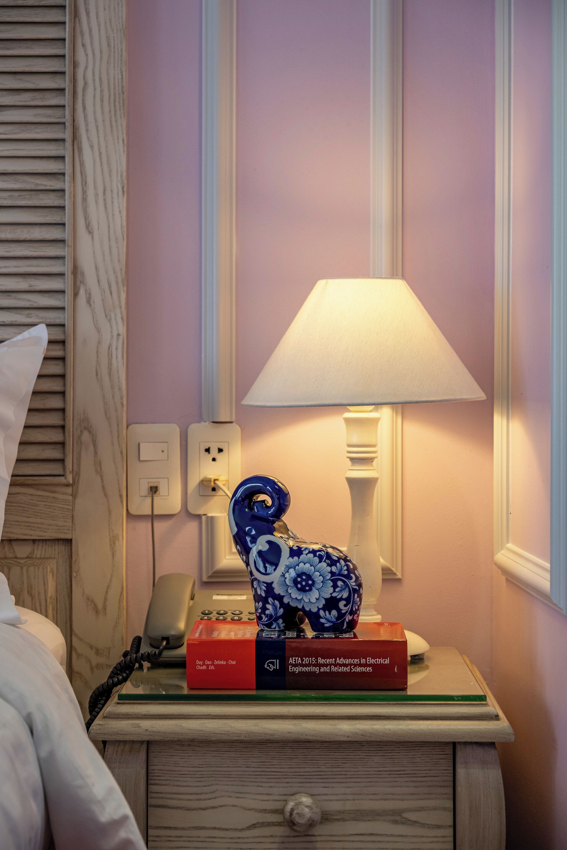 A bedside table with a lamp, a telephone, and books.