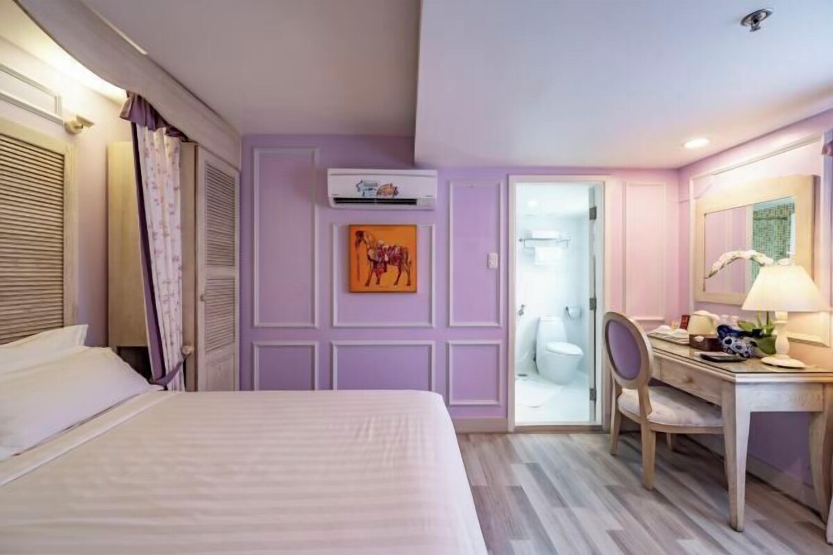 Habitación de hotel con cama, escritorio, silla y baño visible a través de una puerta abierta.