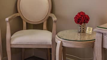 Una stanza con una poltrona in tessuto color beige, un tavolino rotondo con piano in vetro e un vaso con rose rosse. Al di sopra del tavolo, si nota un quadro incorniciato appeso al muro.