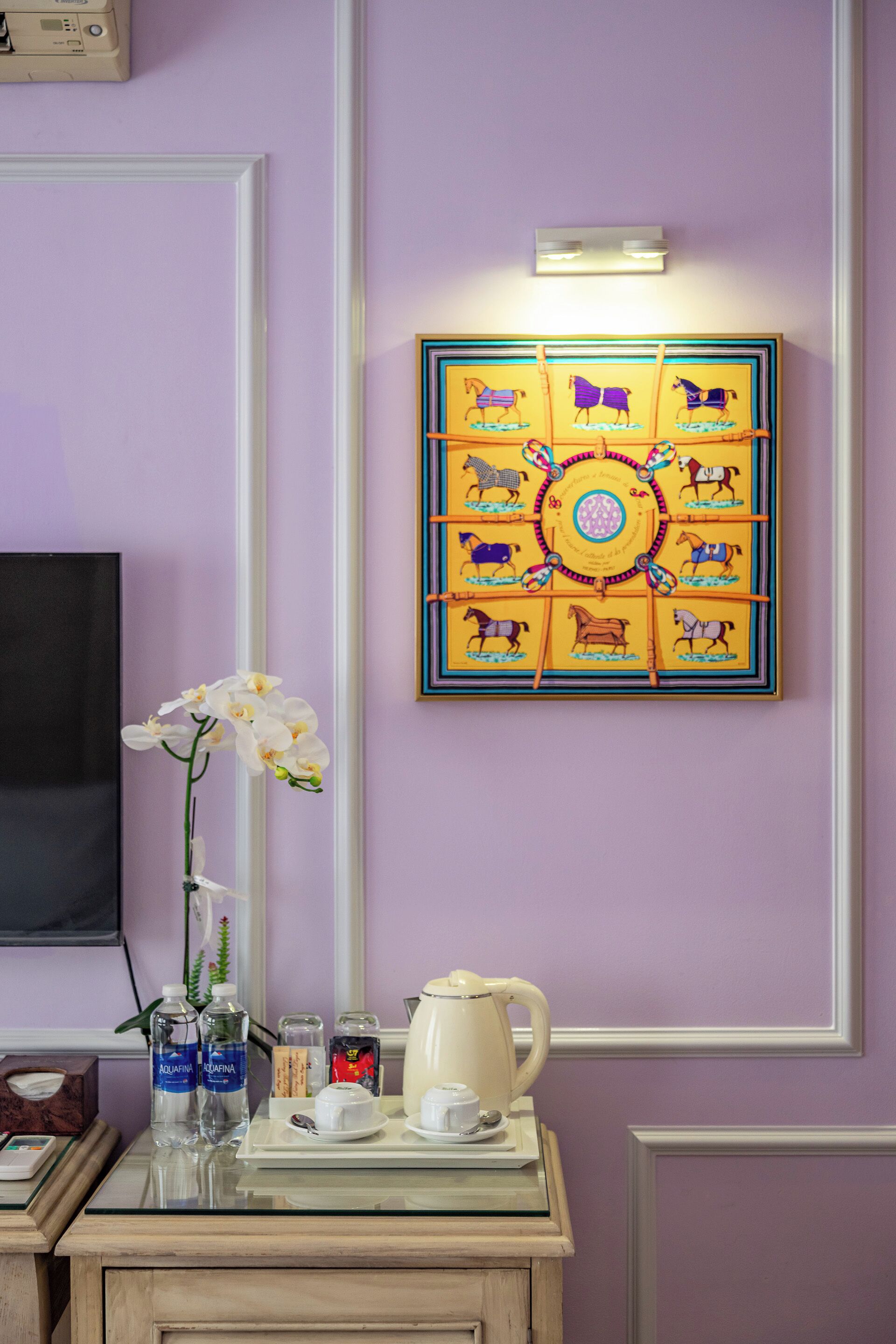 Ein Zimmer mit violettem Wand, einem gerahmten Gemälde mit Pferden, einer Vase mit weißen Blumen und einem Tisch mit Teekanne und Tassen.