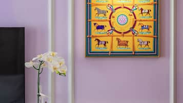 Une pièce avec un mur violet, une œuvre d’art encadrée représentant des chevaux, un vase avec des fleurs blanches et une table avec une théière et des tasses.