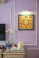 Una habitación con pared morada, una obra de arte enmarcada con caballos, un jarrón con flores blancas y una mesa con tetera y tazas.