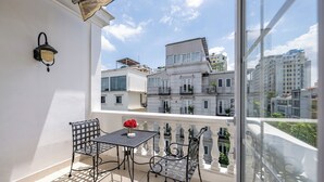 A balcony with a table and chairs, a potted plant, and a view of buildings. - Hotel L Odeon Phu My Hung (Ho Chi Minh City)