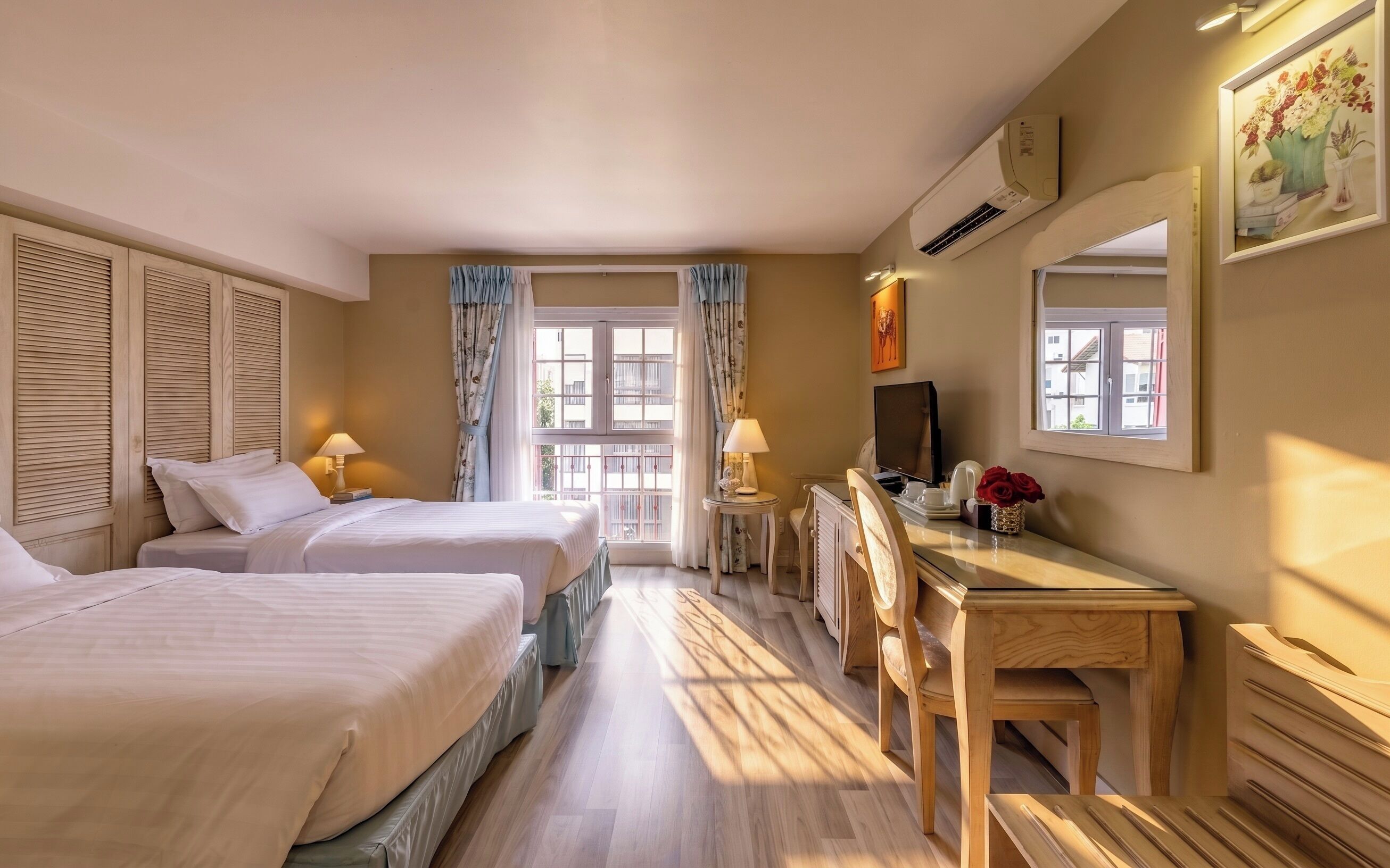 A hotel room with two beds, a desk, a chair, a television, and a window with curtains.