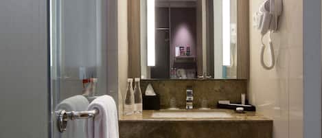A modern bathroom with a glass shower enclosure, a marble sink, a large mirror, and a hairdryer mounted on the wall.