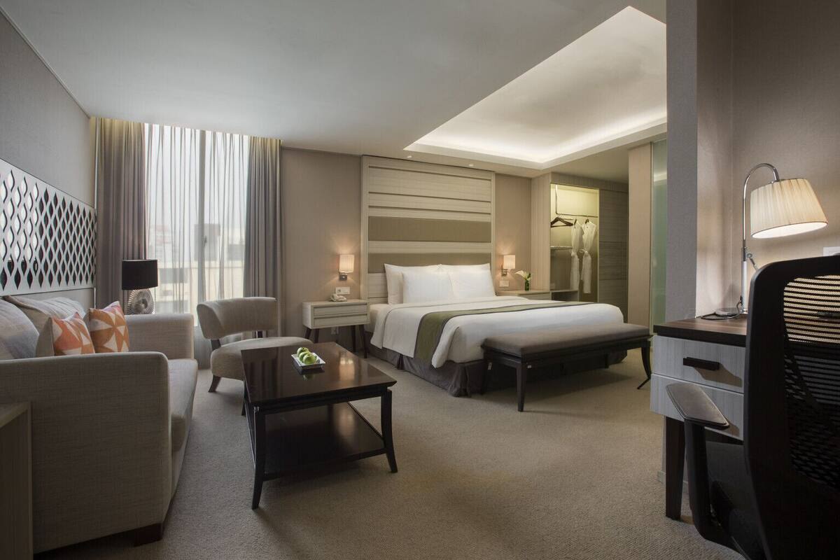 Ein modernes Hotelzimmer mit Bett, Schreibtisch, Sessel, Sofa und kleinem Tisch.