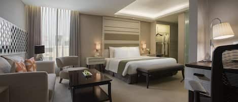 A modern hotel room with a bed, a desk, a chair, a sofa, and a small table.