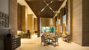 Un hall d’hôtel spacieux, doté d’un plafond haut, de poutres en bois et d’un espace de restauration central avec des tables et des chaises.