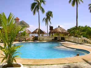 A pool area with lounge chairs, palm trees, and a view of the ocean.