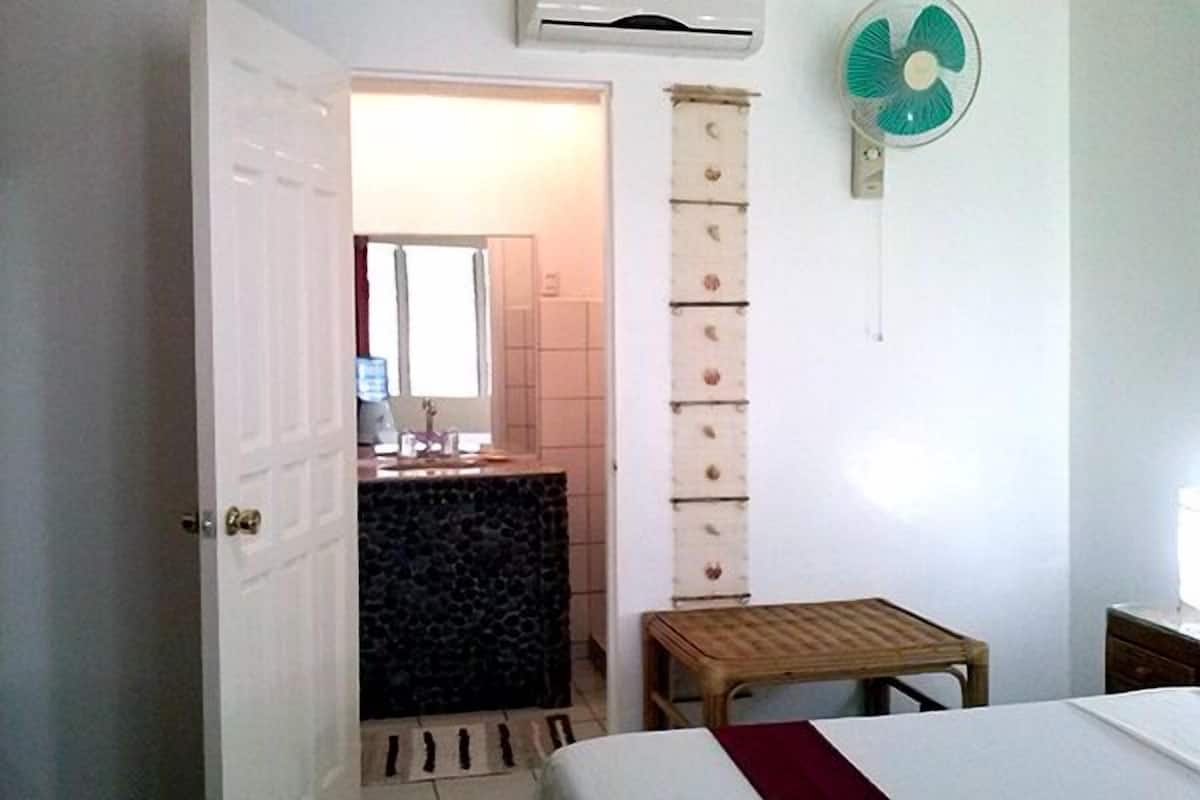 Un dormitorio con una cama, un banco de madera, un aparador, un espejo y un ventilador de pared.