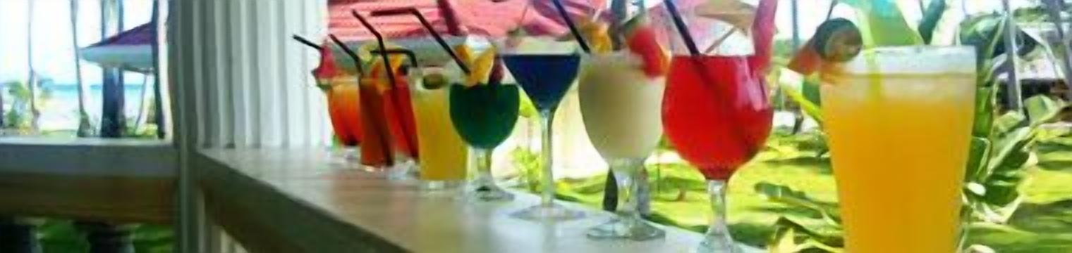 A variety of colorful drinks on a bar counter with a view of the outdoors.