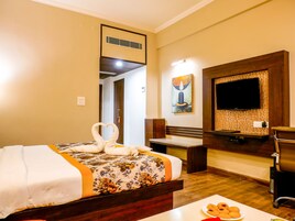 A hotel room with a bed, a television, a desk, and a wall-mounted TV.