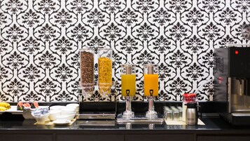 A breakfast bar with coffee, cereal, and orange juice dispensers, a microwave, and a coffee machine.