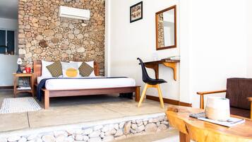 Un dormitorio con pared de piedra, una cama con almohadas estampadas, una mesita de noche de madera, una silla, un escritorio y un espejo.