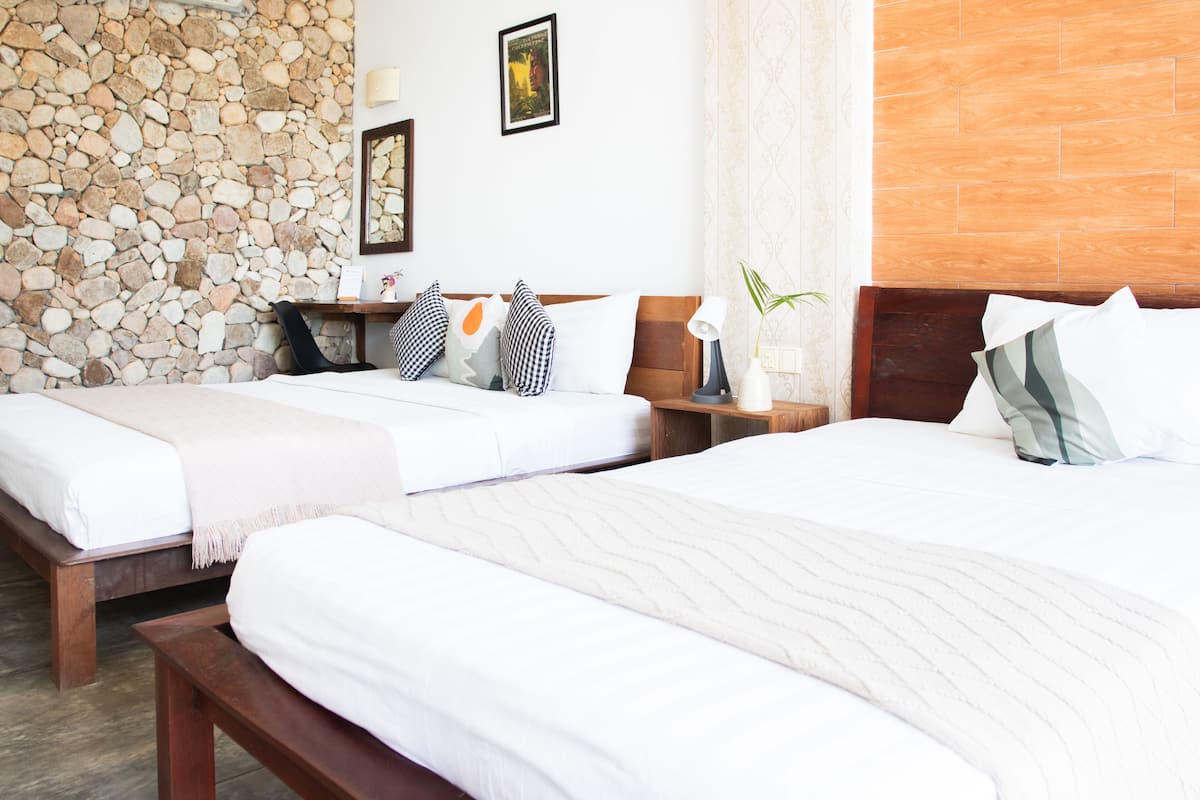 A hotel room with two beds, a stone wall, wooden headboard, and a wooden floor.