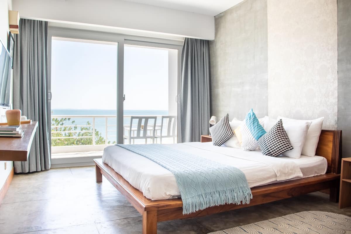 A bedroom with a wooden bed, a view of the sea, and a balcony with curtains.