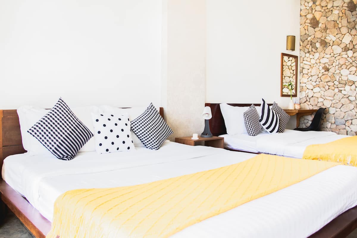 A double bed with a yellow throw blanket, white bedding, and black and white patterned pillows. There is a nightstand with a lamp and a framed picture on the wall.