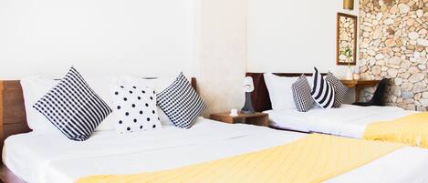 A double bed with a yellow throw blanket, white bedding, and black and white patterned pillows. There is a nightstand with a lamp and a framed picture on the wall.