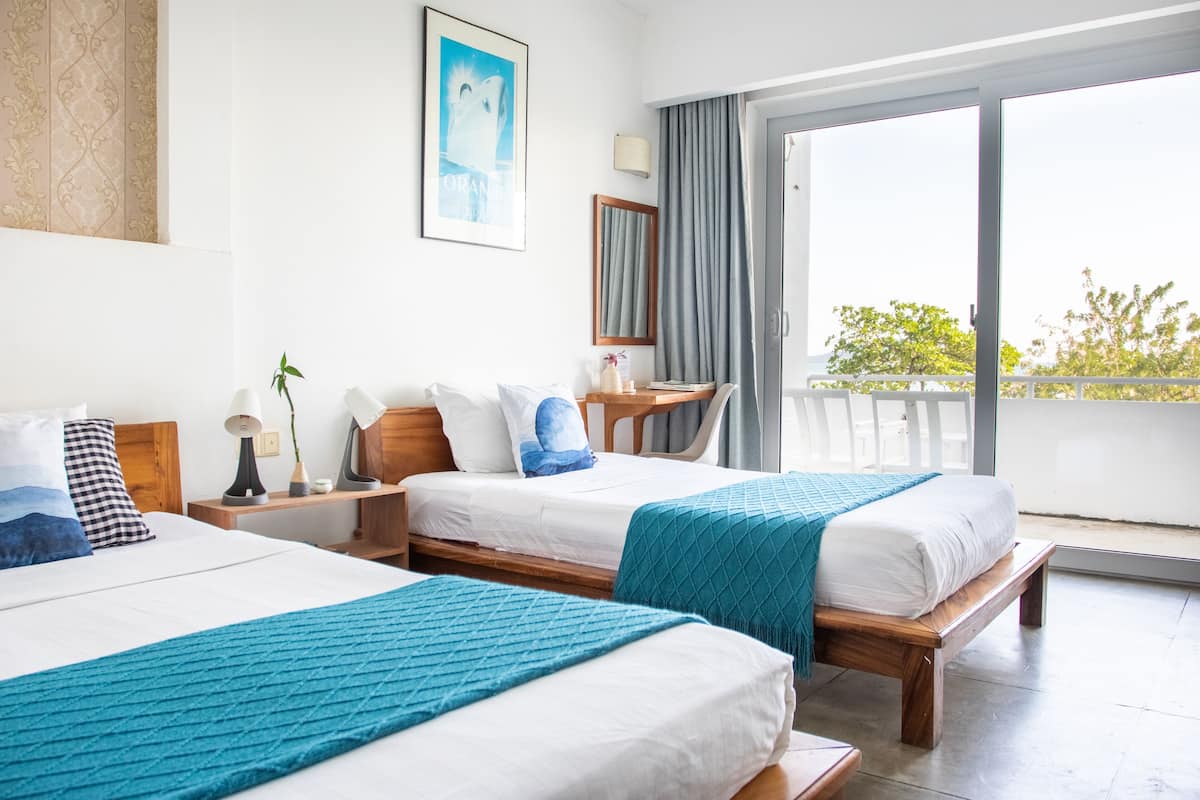 A hotel room with two beds, a balcony, and a view of greenery.