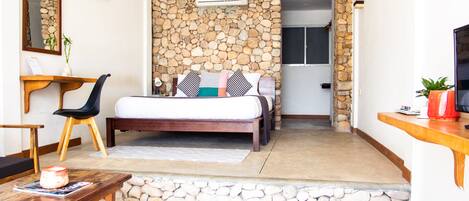 A bedroom with a stone wall, a bed with pillows, a desk, and a chair.