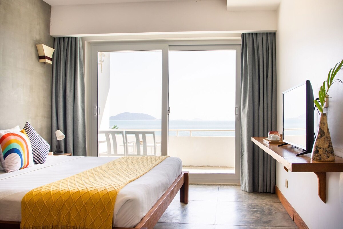 Habitación de hotel con cama, televisor, escritorio y vista al mar.