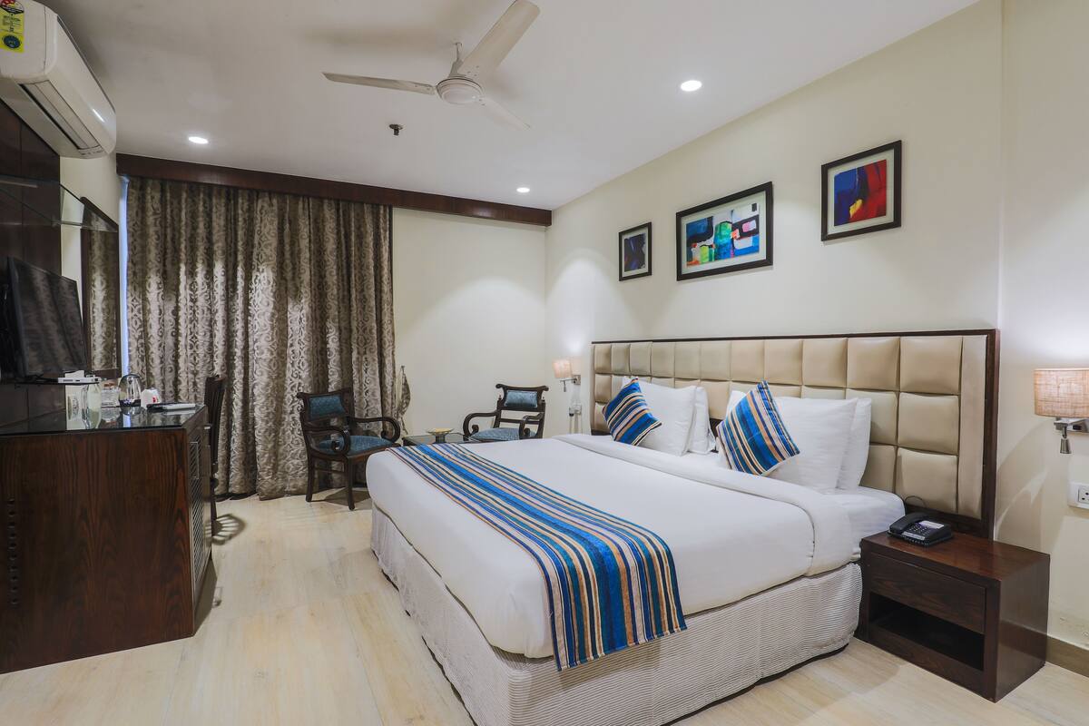 A hotel room with a large bed, a desk, a chair, a ceiling fan, and artwork on the walls.