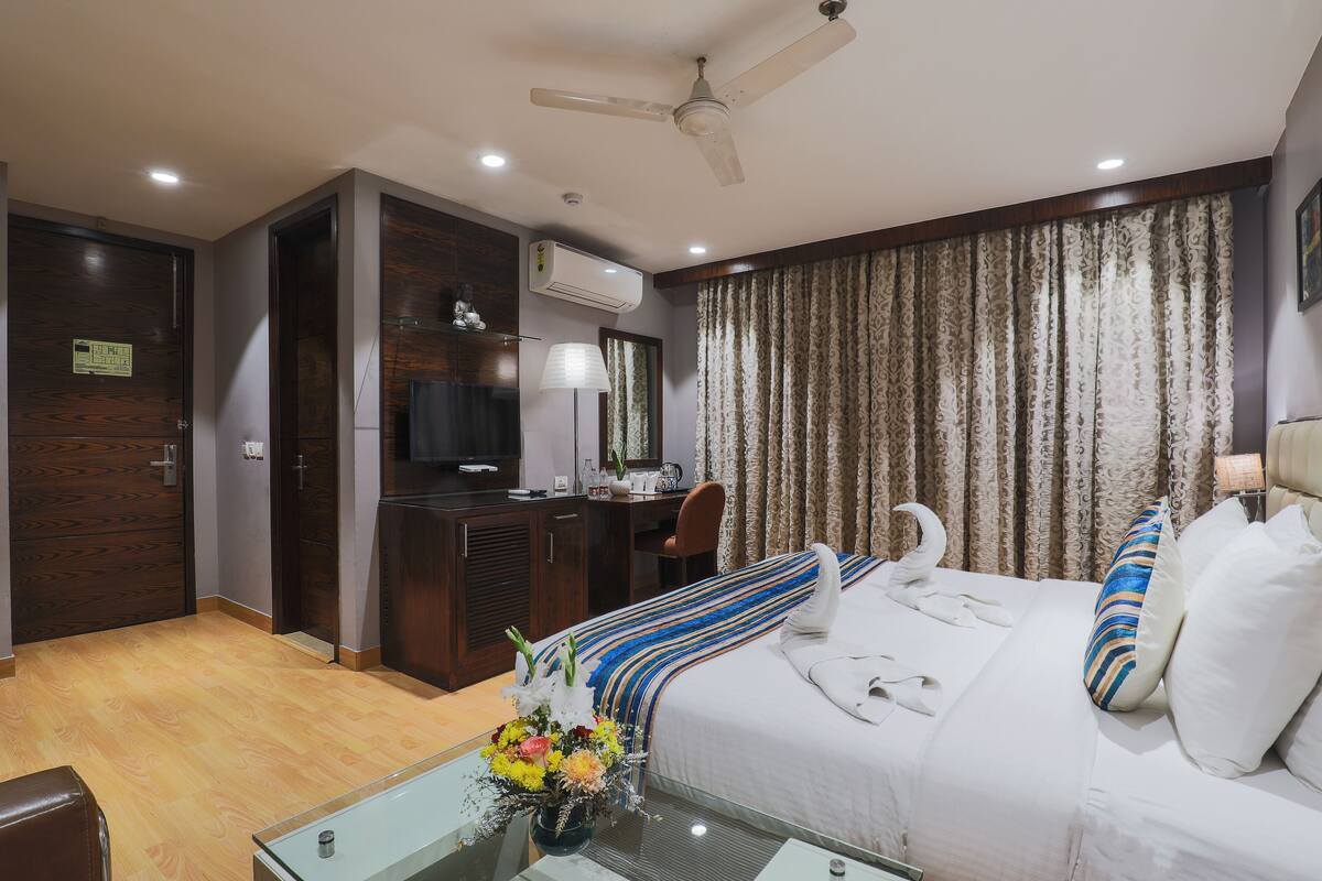 A hotel room with a bed, a desk, a chair, a television, and an air conditioning unit.