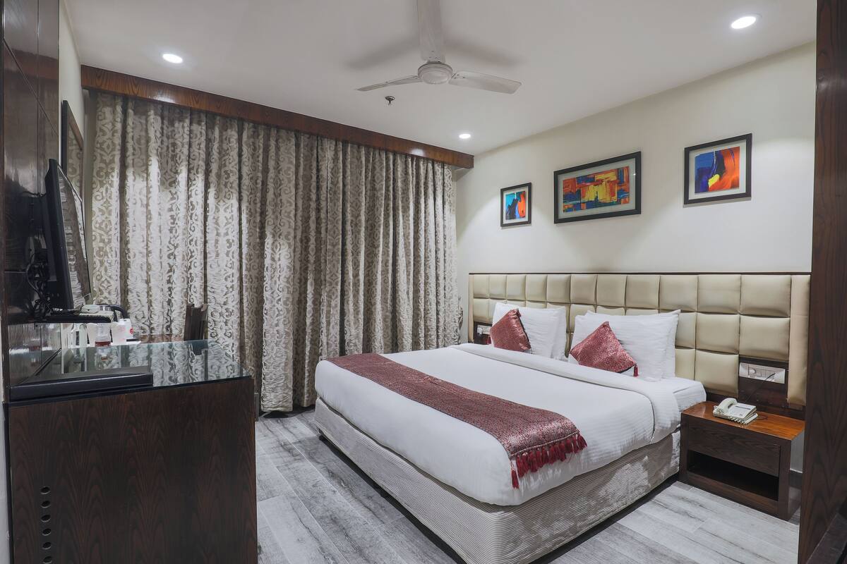 A hotel room with a large bed, a desk with a television, and a ceiling fan.