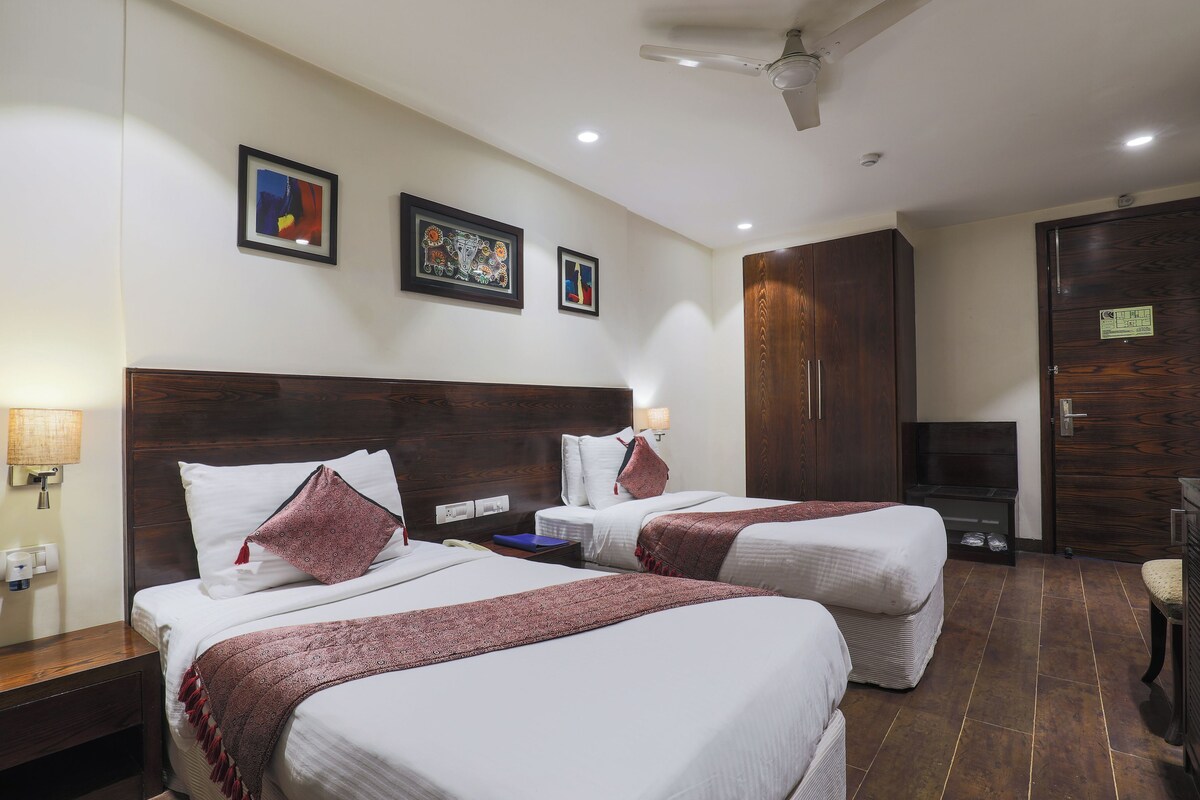 A hotel room with two beds, a wooden wardrobe, a TV, and a ceiling fan.
