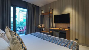 A hotel room with a large bed, a desk with a flat-screen TV, a mirror, and a view of a building outside. - Hotel BlueStone - Nehru Place (New Delhi)