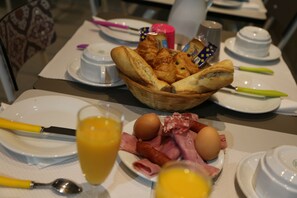 A breakfast table with bread, eggs, ham, and juice. - Hôtel Des Arènes (Paris)