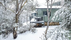 Eine verschneite Landschaft mit einem Haus, das einen Balkon und ein Fundament aus Stein hat.