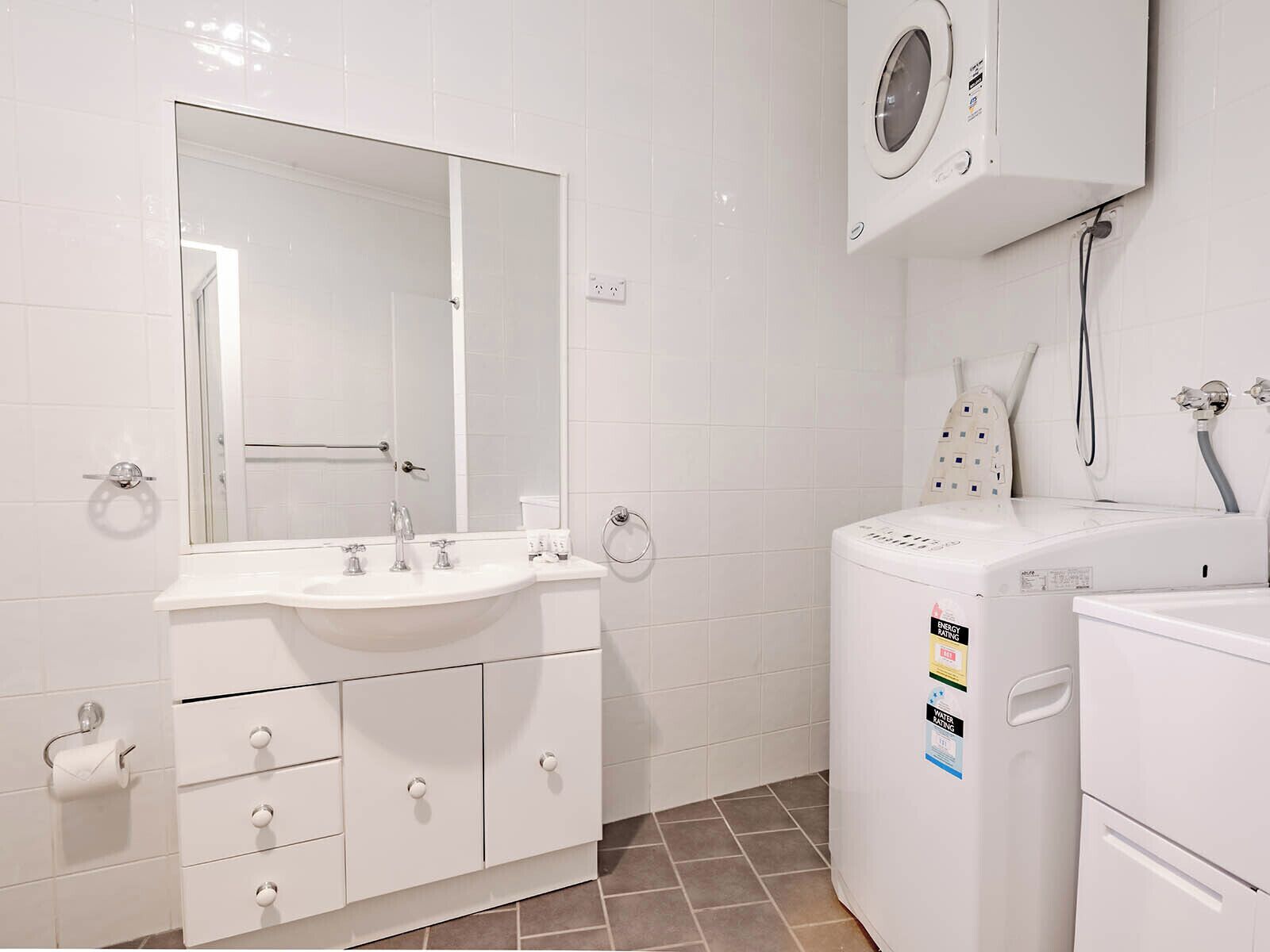 A bathroom with a white sink, mirror, and a white washing machine.