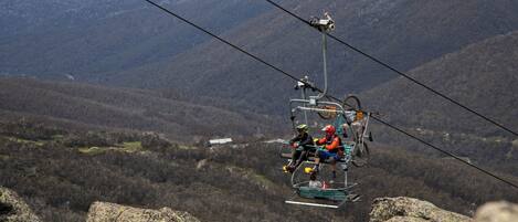 A cable car moving over a mountainous landscape with rocky terrain and sparse vegetation.