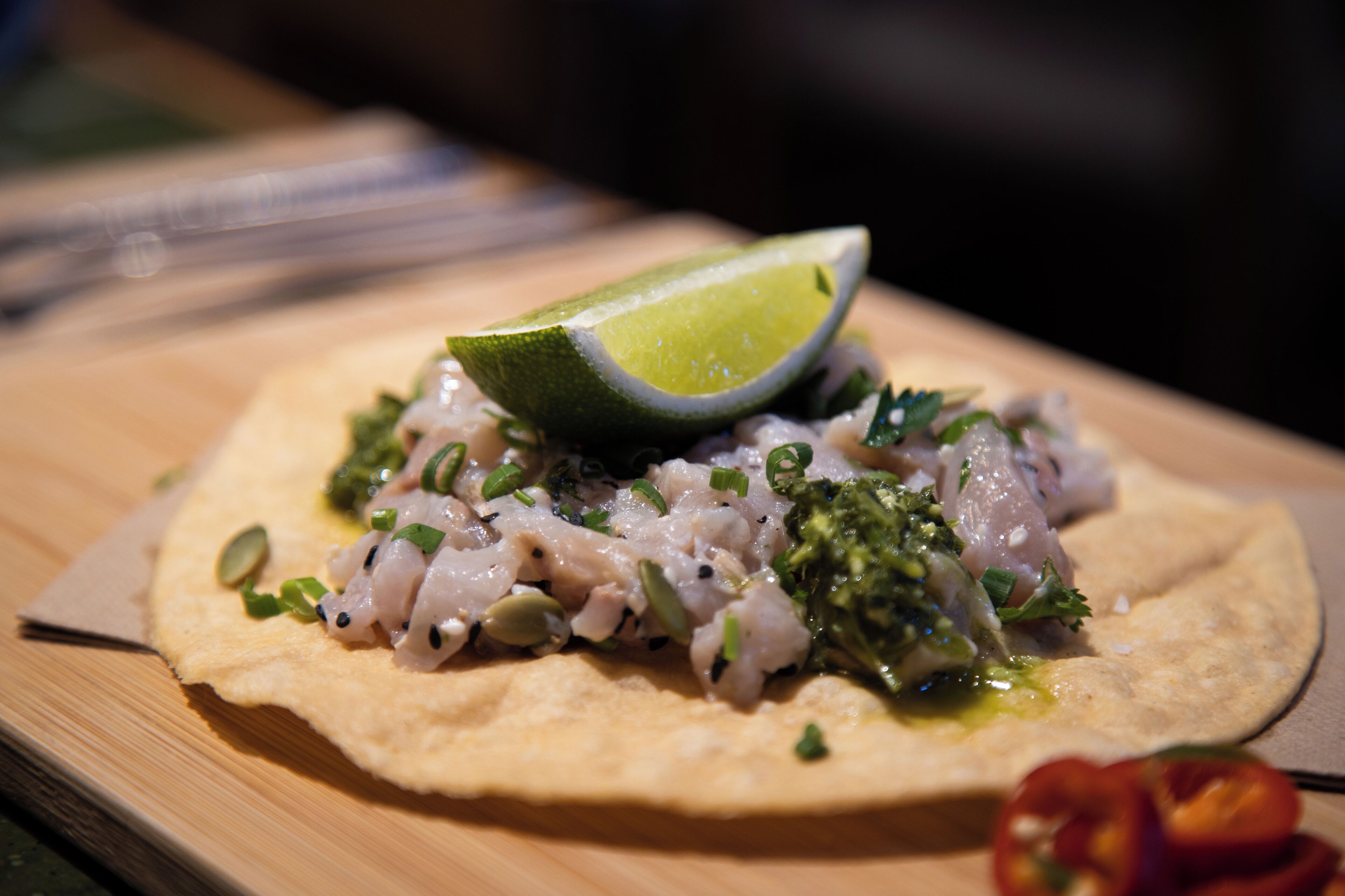 Una focaccia ricoperta di un piatto di pesce, guarnita con erbe aromatiche e una fetta di lime.