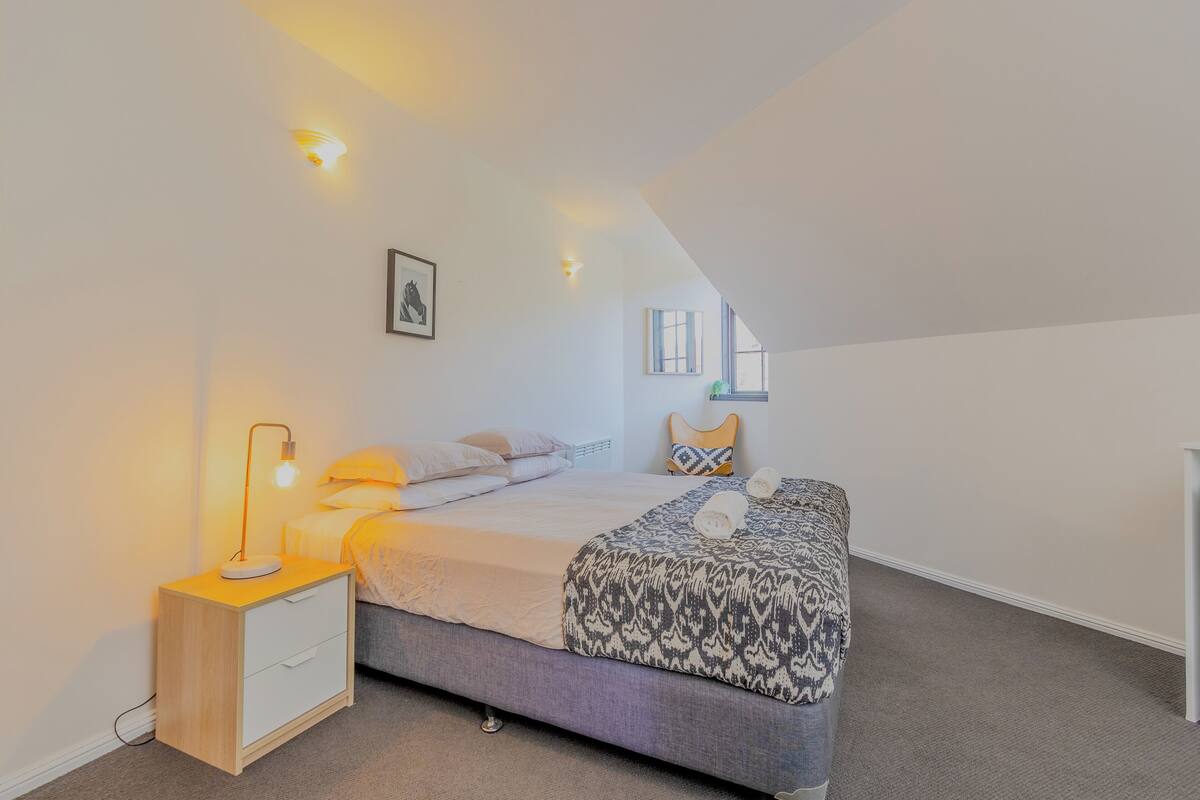 A bedroom with a bed, bedside table, lamp, and a window.