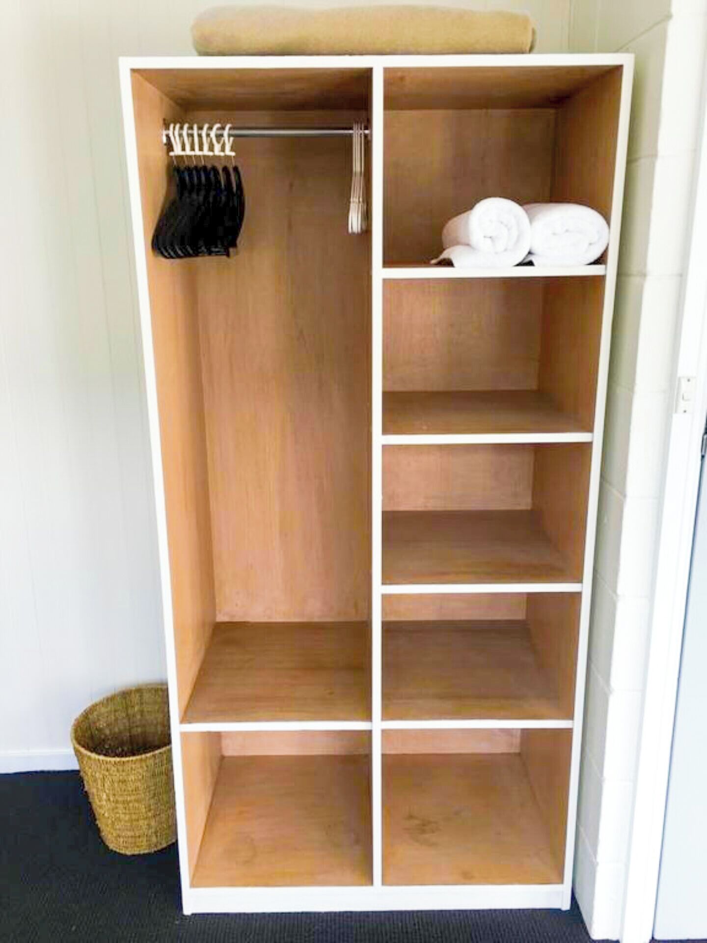A wooden wardrobe with multiple shelves and hanging space, a basket, and a towel on top.