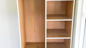 A wooden wardrobe with multiple shelves and hanging space, a basket, and a towel on top.