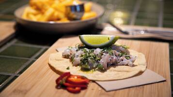 A wooden table with a plate of fish tacos, a lime wedge, and a small bowl of fries.