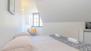 Un dormitorio con cama, una silla, televisor y ventana.