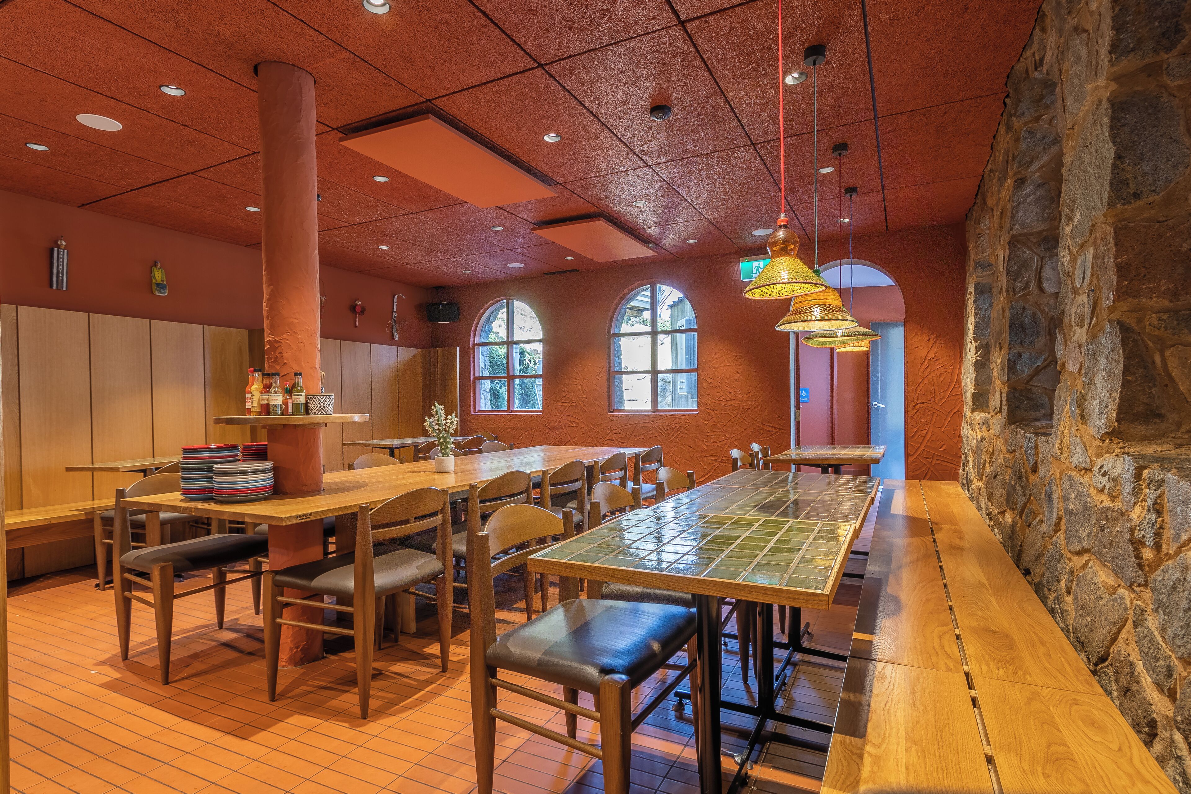 A restaurant with wooden tables and chairs, a stone wall, and arched windows.